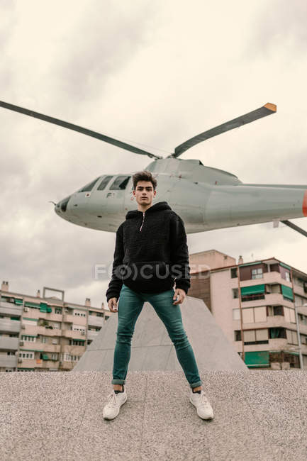 Joven guapo parado frente al monumento del helicóptero en la calle de la ciudad - foto de stock