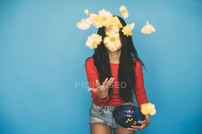 Junge Frau steht und wirft Blumen auf blauem Hintergrund — Stockfoto