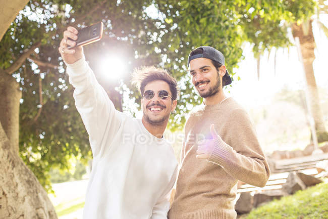 Усміхнені щасливі чоловіки друзі беруть селфі зі смартфоном у сонячному парку — стокове фото