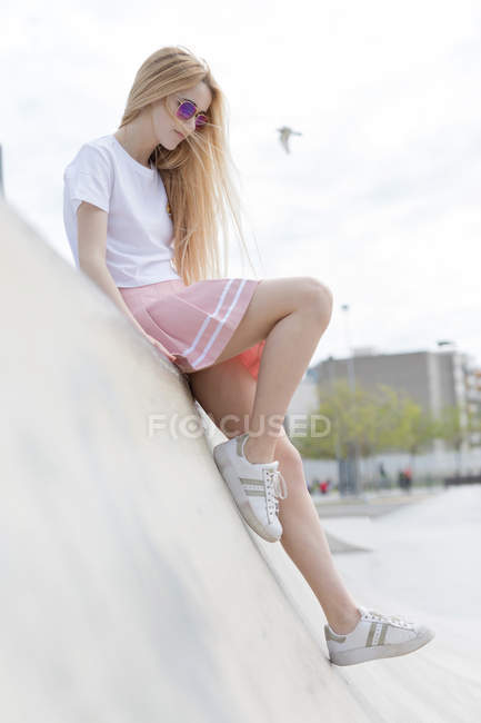 Stylish blonde girl in sunglasses sitting on skate park — Stock Photo