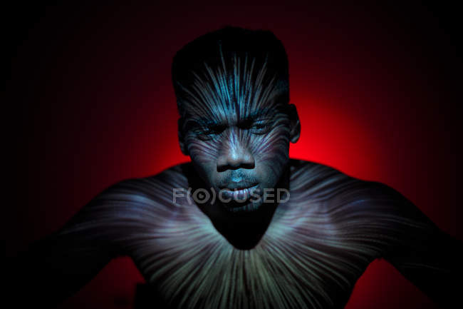 Homem étnico sem emoção de pé com linhas de luz no corpo e olhando para a câmera — Fotografia de Stock