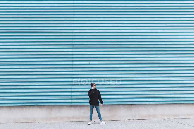 Молодой подросток, стоящий у металлической стены и разговаривающий по мобильному телефону — стоковое фото
