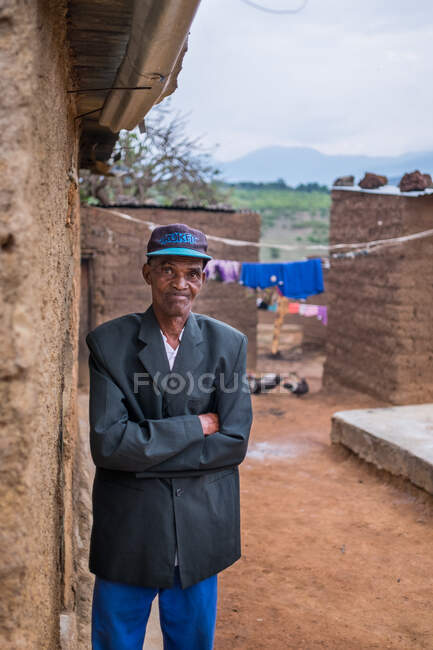ANGOLA - ÁFRICA - 5 de abril de 2018 - Homem étnico adulto idoso de pé de braços cruzados na casa da aldeia e olhando para a câmera. — Fotografia de Stock