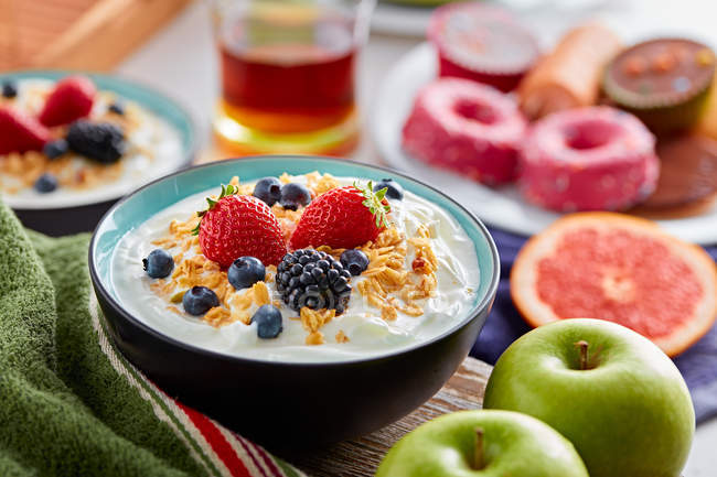 Tazón de desayuno de yogur y bayas en la mesa con ingredientes - foto de stock