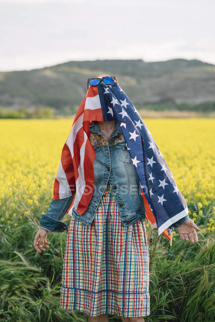 Lady in casual clothes staying in yellow field with sunglasses over American flag with sunlight — Stock Photo