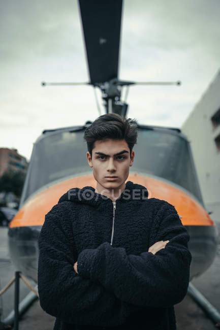 Jovem de pé com braços cruzados com monumento de helicóptero no fundo — Fotografia de Stock