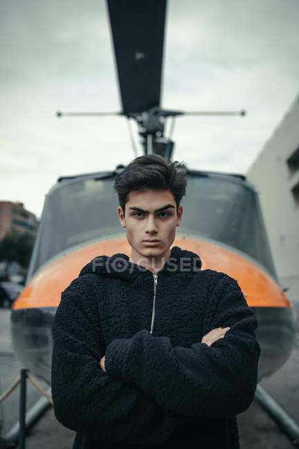 Joven de pie con los brazos cruzados con el monumento del helicóptero en el fondo - foto de stock