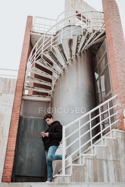 Young handsome man standing on shabby stairs and using mobile phone — Stock Photo