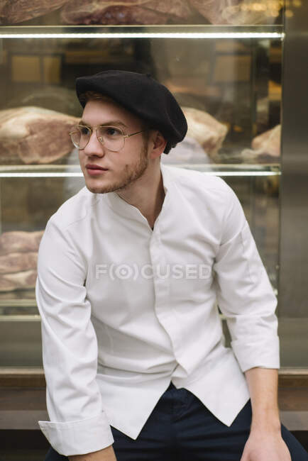Hombre joven en elegante chaqueta blanca y gorra con gafas de moda y mirando a la cámara. - foto de stock
