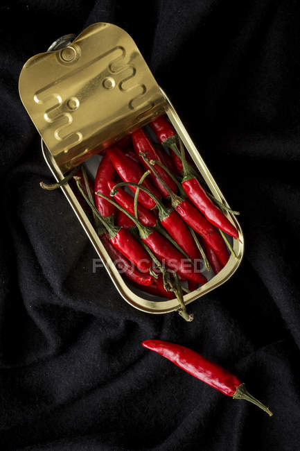 Tin can with bunch of hot chili peppers on black fabric — Stock Photo
