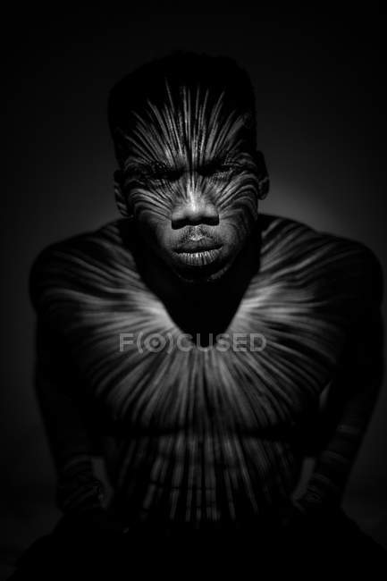 Homem étnico sem emoção de pé com linhas de luz no corpo e olhando para a câmera — Fotografia de Stock