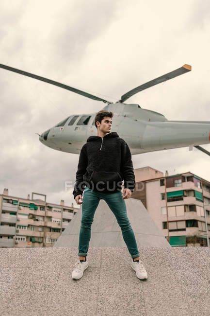 Bel giovanotto in piedi di fronte al monumento elicottero sulla strada della città — Foto stock