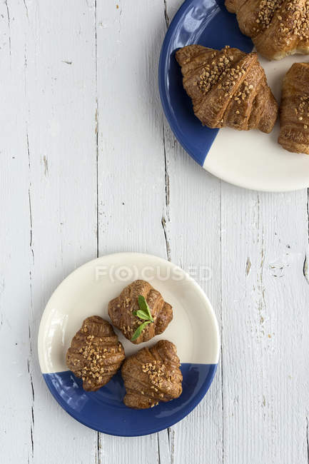 Croissants cuits au four sur assiettes blanches et bleues sur table blanche en bois — Photo de stock