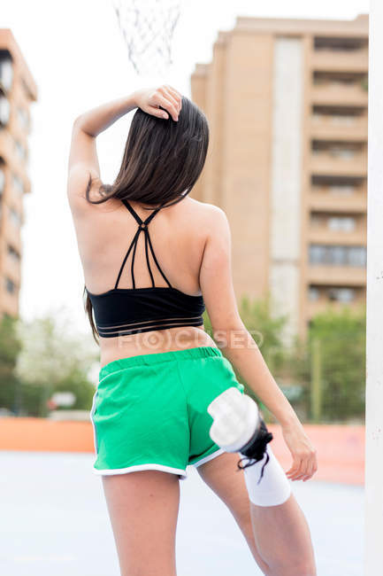 Back view of slim woman in sportswear exercising on outdoors sports ground in city — Stock Photo