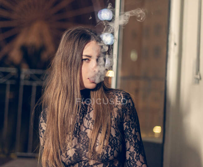 Bonita morena en encaje seductor vestido de fumar narguile sensualmente sentado en el suelo con los ojos cerrados - foto de stock