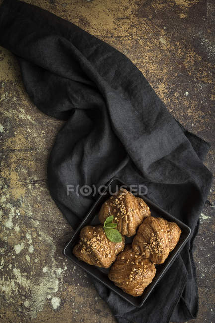 Croissants horneados en plato sobre tela negra sobre superficie oscura malhumorada - foto de stock