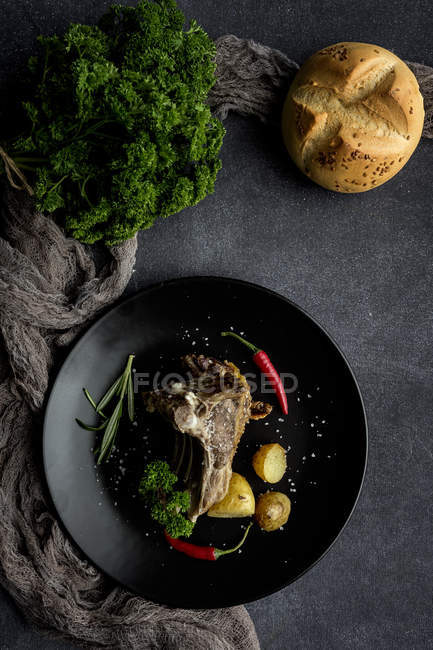 Cordeiro assado com batatas em prato preto com pão e salsa — Fotografia de Stock