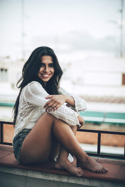 Portrait d'une jeune femme souriante assise au balcon — Photo de stock