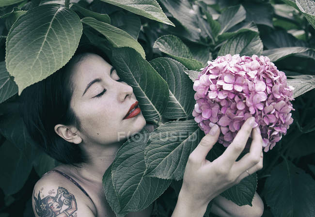 Sensual young woman touching pink flower growing on bush — Stock Photo