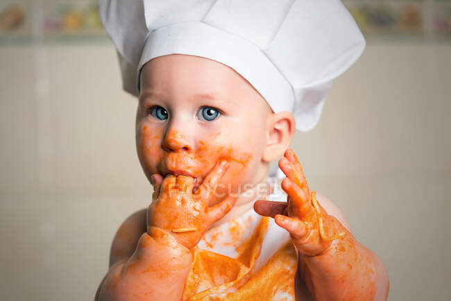 Garçon joyeux tout-petit dans le tablier avec le visage sale recouvert de sauce. — Photo de stock