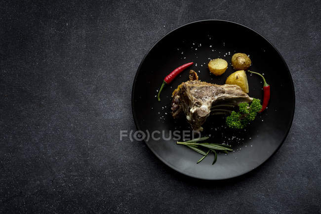 Roast lamb with potatoes on black plate on grey background — Stock Photo
