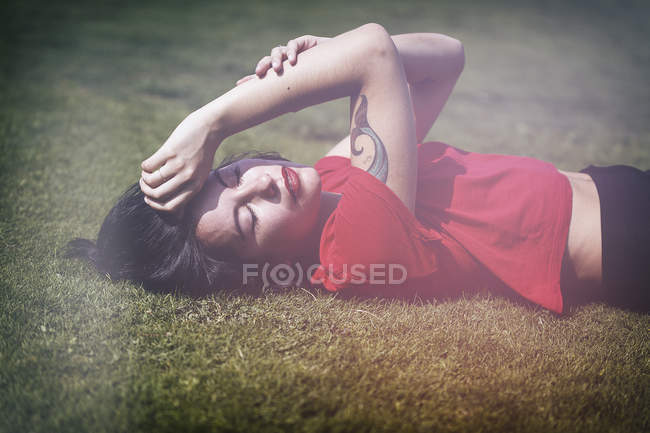 Sensual hipster girl in red t-shirt lying on grass — Stock Photo