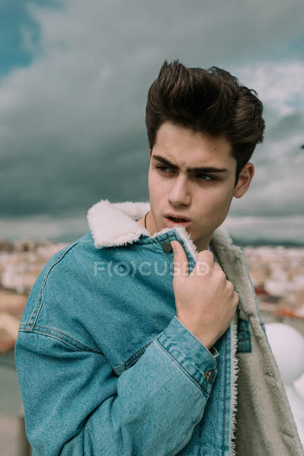 Retrato de adolescente joven en chaqueta de mezclilla con estilo de pie en el fondo de la ciudad - foto de stock