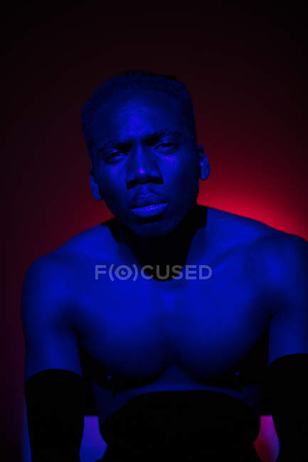 Безэмоциональный этнический мужчина, стоящий со светом на теле и смотрящий в камеру — стоковое фото