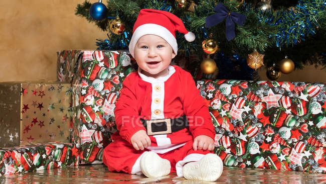 Портрет счастливого мальчика в костюме Санта-Клауса, сидящего за елкой — стоковое фото