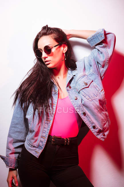 Bella giovane donna vestita di rosa con gli occhiali da sole in piedi al muro bianco — Foto stock