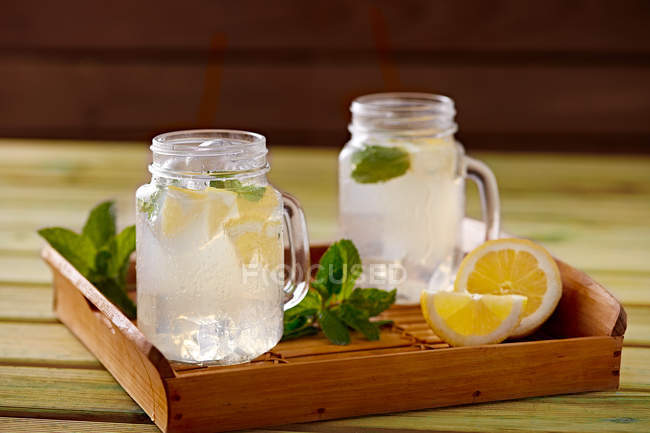 Wooden tray with glass cups of cooling lemonade made of lemon and mint — Stock Photo