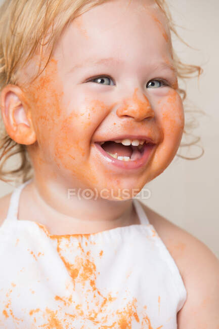 Веселий маленький хлопчик в фартусі з брудним обличчям, вкритим соусом . — стокове фото