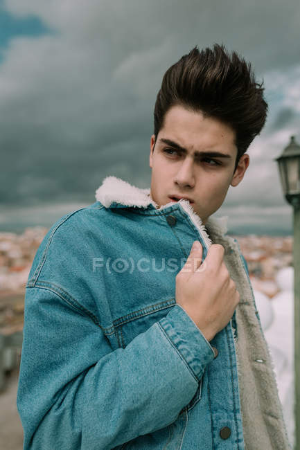 Retrato de adolescente joven en chaqueta de mezclilla con estilo de pie en el fondo de la ciudad - foto de stock
