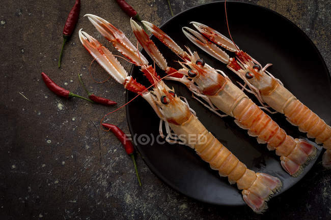 Plate of boiled shrimps on rustic tabletop with small chilies — Stock Photo