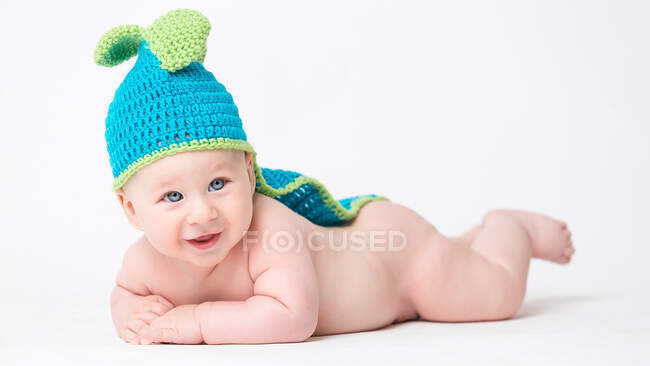 Adorable naked little boy in blue knitted hand lying on blue background. — Stock Photo