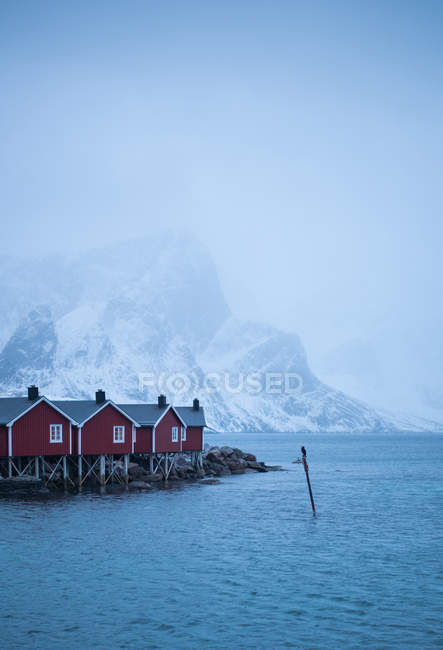 Blue water of sea with red wooden cabins on shore and misty mountains on background — Stock Photo