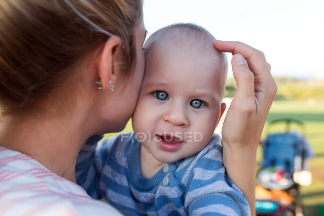 Чарівний маленький хлопчик сидить на руках матері і дивиться на камеру . — стокове фото