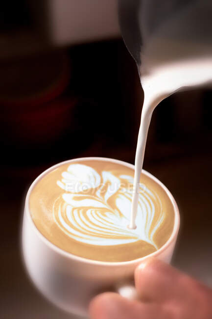 Cortar la mano de camarero irreconocible verter crema al café con leche y dibujar una flor. - foto de stock
