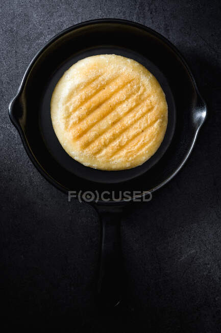 View from above of colombian food Arepa in black frying pan on dark background — Stock Photo