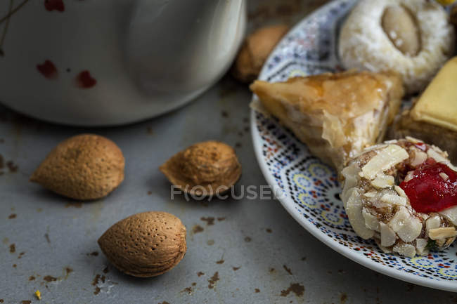 Dolci tipici marocchini con miele su piatto su tavola grigia con mandorle intere — Foto stock