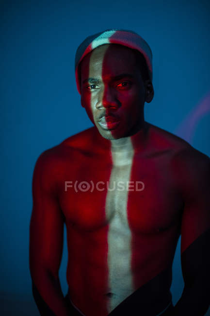 Emotionless ethnic man standing with light line on body and looking at camera — Stock Photo