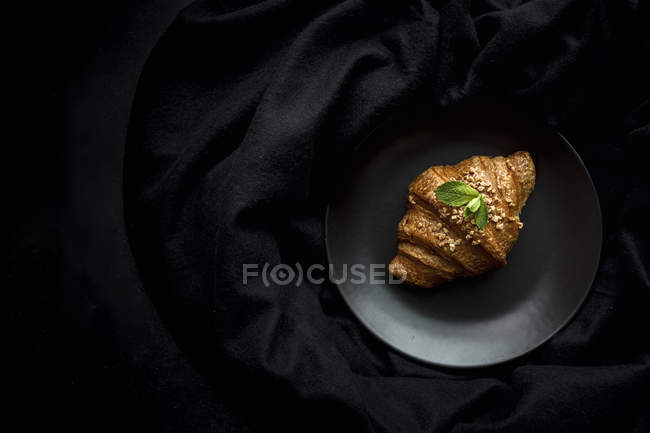Croissant al forno su piatto su tessuto nero — Foto stock