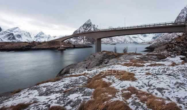 Vista pitoresca de montanhas nevadas e mar com ponte sobre fundo — Fotografia de Stock