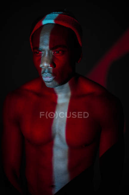Homem étnico sem emoção de pé com linha de luz no corpo e olhando para longe — Fotografia de Stock