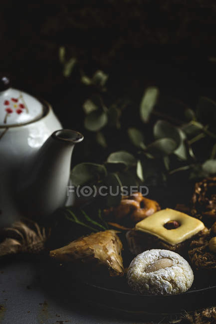 Typical Moroccan sweets with honey and almonds on plate with teapot on dark background — Stock Photo