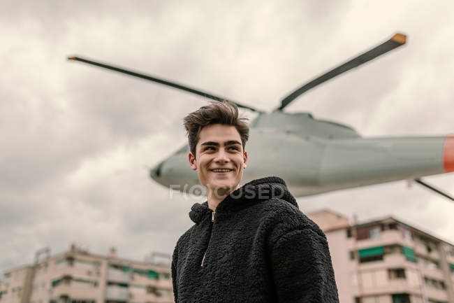 Смеющийся молодой человек, стоящий у памятника вертолету на городской улице — стоковое фото