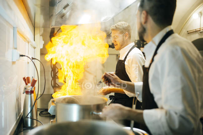 Щасливого кухаря, роблячи це фламбе кухні ресторану з колега спостерігаючи — стокове фото
