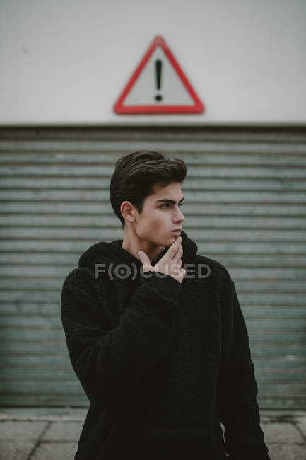 Adolescente pensieroso in giacca nera con cappuccio in piedi sulla strada con segno esclamativo e guardando altrove — Foto stock