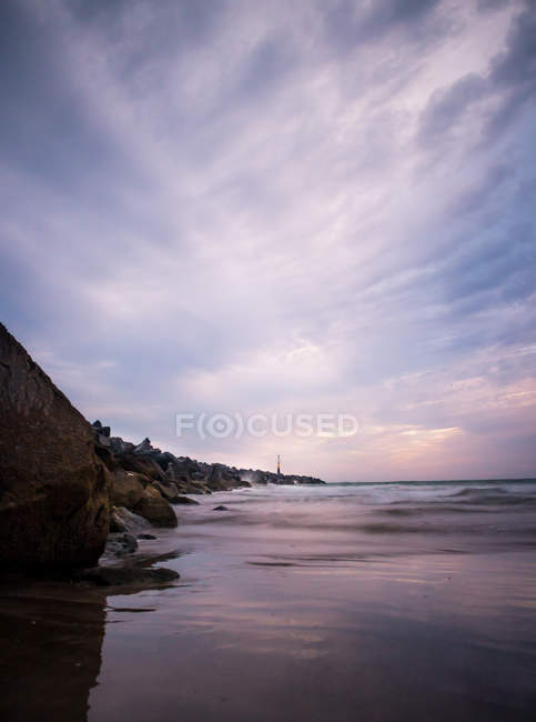 Falaise rocheuse et l'eau de mer sous ciel nuageux coucher de soleil dramatique — Photo de stock