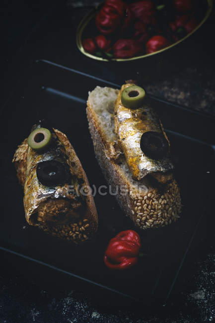 Tranches de pain avec du poisson en conserve et des olives sur une plaque à pâtisserie près du piment fort — Photo de stock